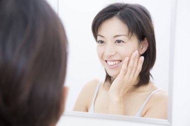 Asyalı kadın banyoda ayna kullanıyor. 