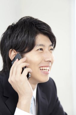 Gülümseyen Asyalı genç adam telefonda konuşuyor.