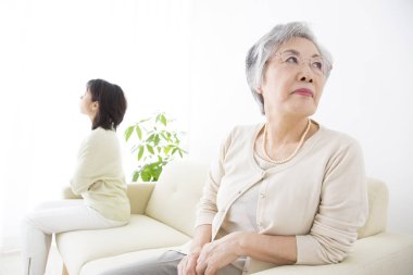 Yaşlı Asyalı kadın ve yetişkin kızı kanepede oturuyorlar. 