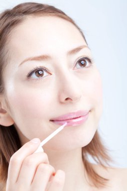 Genç ve güzel bir kadın beyaz arka plana ruj sürüyor.