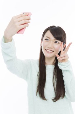 Beyaz arka planda akıllı telefonlu bir kadın selfie çekiyor. 