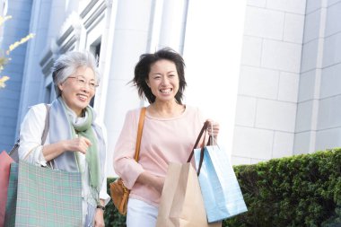 İki kadın alışveriş torbalarıyla kaldırımda yürüyorlar.