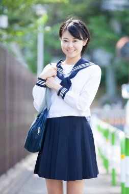 Gülümseyen Japon kız öğrenci üniforması içinde sokakta poz veriyor.