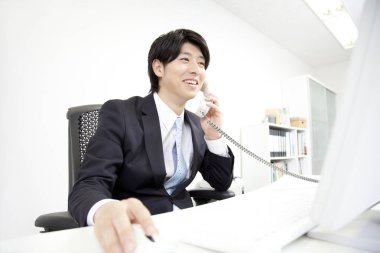 gülümseyen Asyalı işadamı iş yerinde telefonla konuşuyor