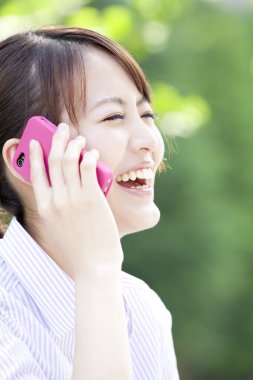 Parkta cep telefonu olan genç bir kadın.