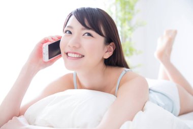 Genç bir kadın yatak odasında cep telefonuyla konuşuyor. 