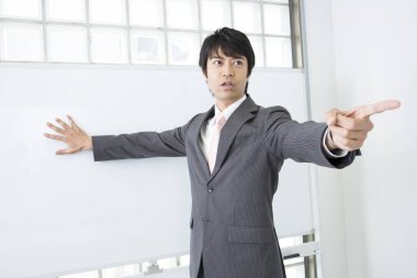 Japanese teacher in casual suit giving a lecture, standing close to blackboard  clipart