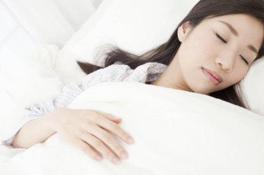 Genç Asyalı kadın yatakta uyuyor.