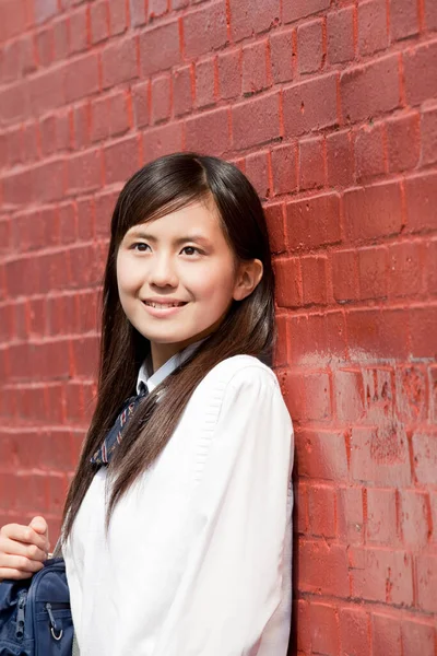Genç Asyalı kadın tuğla duvarın önünde.