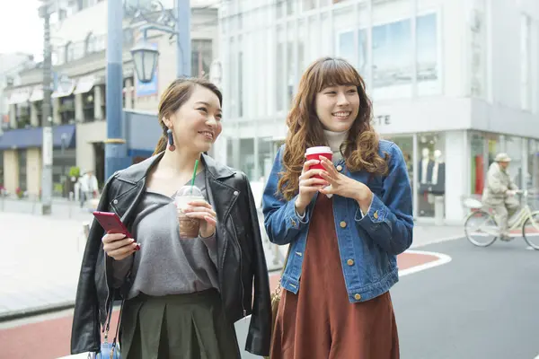 two young women with coffee  walking in city