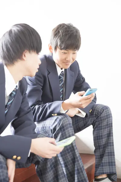 两名身穿校服的亚洲男孩使用手机 — 图库照片