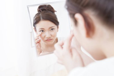 Asyalı kadın aynaya bakıyor.