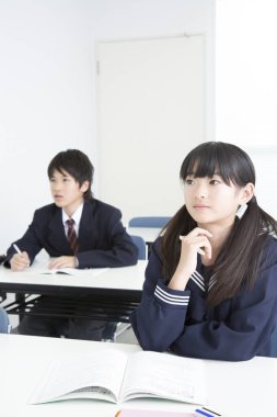 Asyalı çocuklar sınıftaki masalarda ders çalışıyorlar.