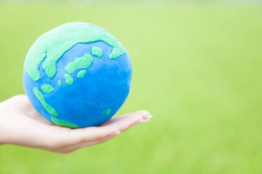 Yeşil arka planda kilden yapılmış basit bir küreyi tutan bir el. 