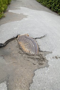 Zarar görmüş asfalt yol, metal rögar kapağı yüzeyi açığa çıkarıyor.