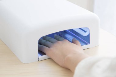 UV tırnak kurutma makinesi kullanan bir kadın.