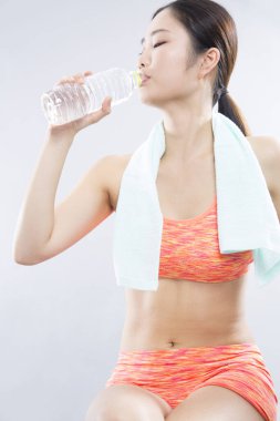 Beyaz arka planda izole edilmiş egzersiz sonrası su içen genç Asyalı kadın.