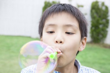 Çocuk çimenlere sabun köpüğü üflüyor.