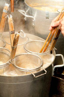 Mutfakta metal süzgeçler kullanarak erişte kaynatmak.