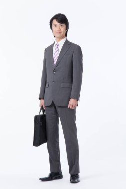 Asyalı işadamı elinde evrak çantasıyla kameraya bakıyor. 