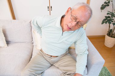 Sırtı ağrıyan Asyalı son sınıf öğrencisi, kanepede oturuyor.