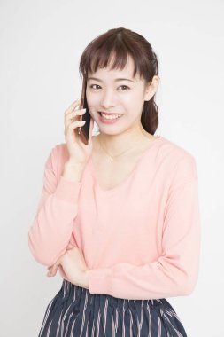 Pembe kazaklı genç Japon kadının beyaz arka planda akıllı telefonuyla konuşmasının stüdyo portresi. 