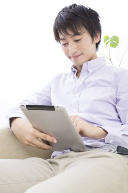 Genç adam odasında tablet kullanıyor.