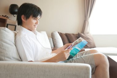 Genç adam kanepede kitap okuyor.