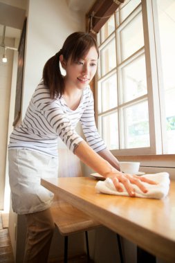 Genç Asyalı kadın mutfaktaki masayı temizliyor.