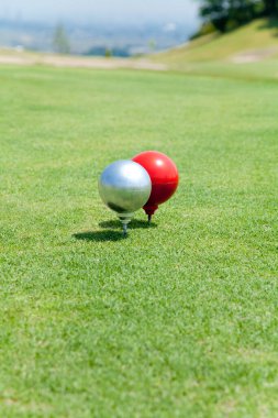 Gümüş ve kırmızı golf toplarını yeşil çimlere yakın tut. 