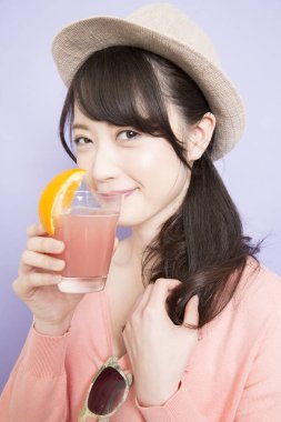 Bir bardak taze meyve suyuyla şapkalı güzel Asyalı kadının stüdyo fotoğrafı.