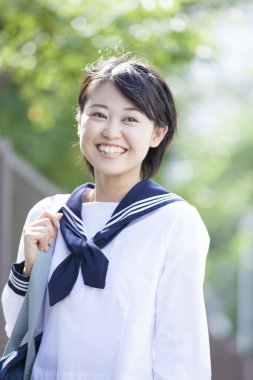 gülümseyen Japon kız öğrenci üniformalı parkta poz veriyor.