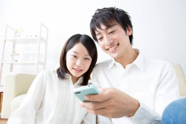 Bir adam ve bir kadın koltukta oturup cep telefonuna bakıyorlar.