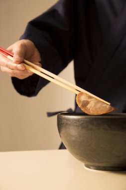 Yemek çubuklarını kullanarak kasenin üzerinde köfte tutarak.