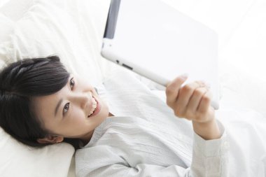 Yatakta dijital tabletle yatan gülümseyen kız.