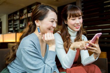 İki mutlu Asyalı arkadaş restoranda akıllı telefon kullanıyor.