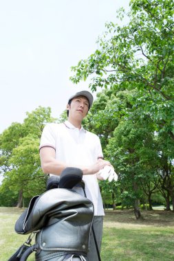 Dışarıda golf çantalı Asyalı bir adam.