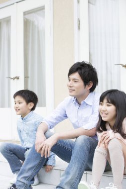 Genç Asyalı bir aile evinin merdivenlerinde oturuyor. 