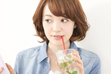 Genç Japon kadın limonlu ferahlatıcı su içerken elinde akıllı telefon tutuyor.