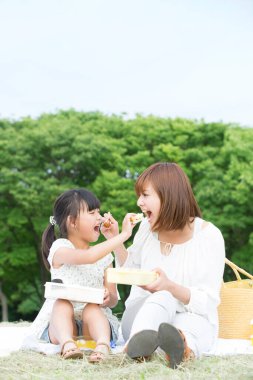 Anne ve kızı çimenlerde yemek yiyor. 