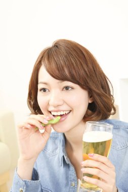 Neşeli Japon kadın evde yeşil bezelyeyle bira içiyor.