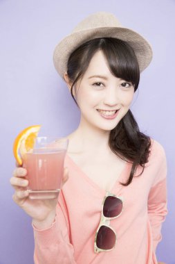 Bir bardak taze meyve suyuyla şapkalı güzel Asyalı kadının stüdyo fotoğrafı.