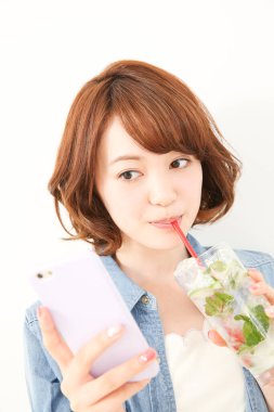 Genç Japon kadın limonlu ferahlatıcı su içerken elinde akıllı telefon tutuyor.