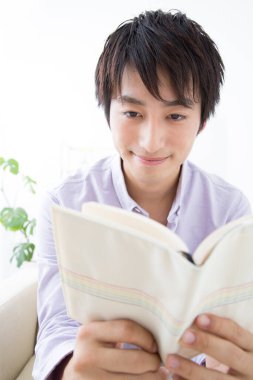 Genç adam evde kitap okuyor.