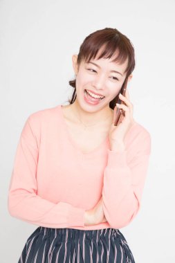 Asyalı genç bir kadın beyaz arka planda cep telefonuyla konuşuyor. 