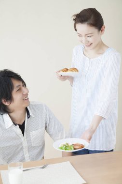 Genç Asyalı kadın erkeğine kahvaltı servisi yapıyor.