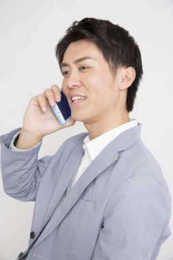 Asyalı işadamı beyaz arka planda izole edilmiş cep telefonu kullanıyor