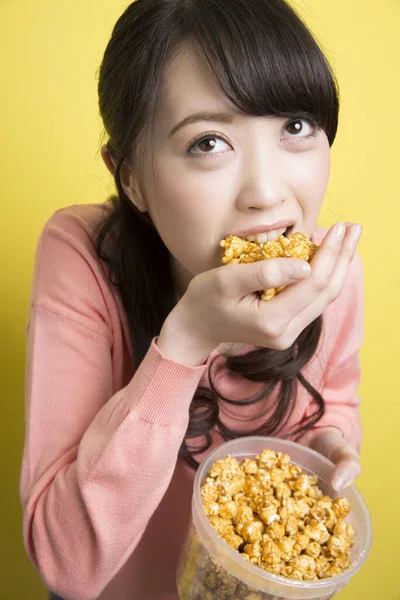黄色の背景にポップコーンを食べるアジアの女性の肖像画 — ストック写真