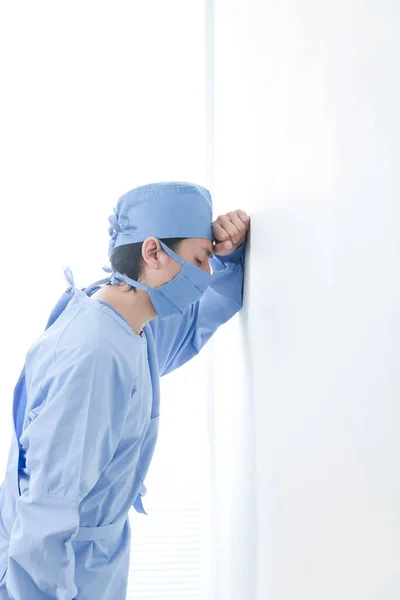 young sad  doctor wearing mask standing by wall