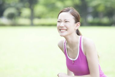 Gülümseyen Asyalı kadın parkta koşuyor.